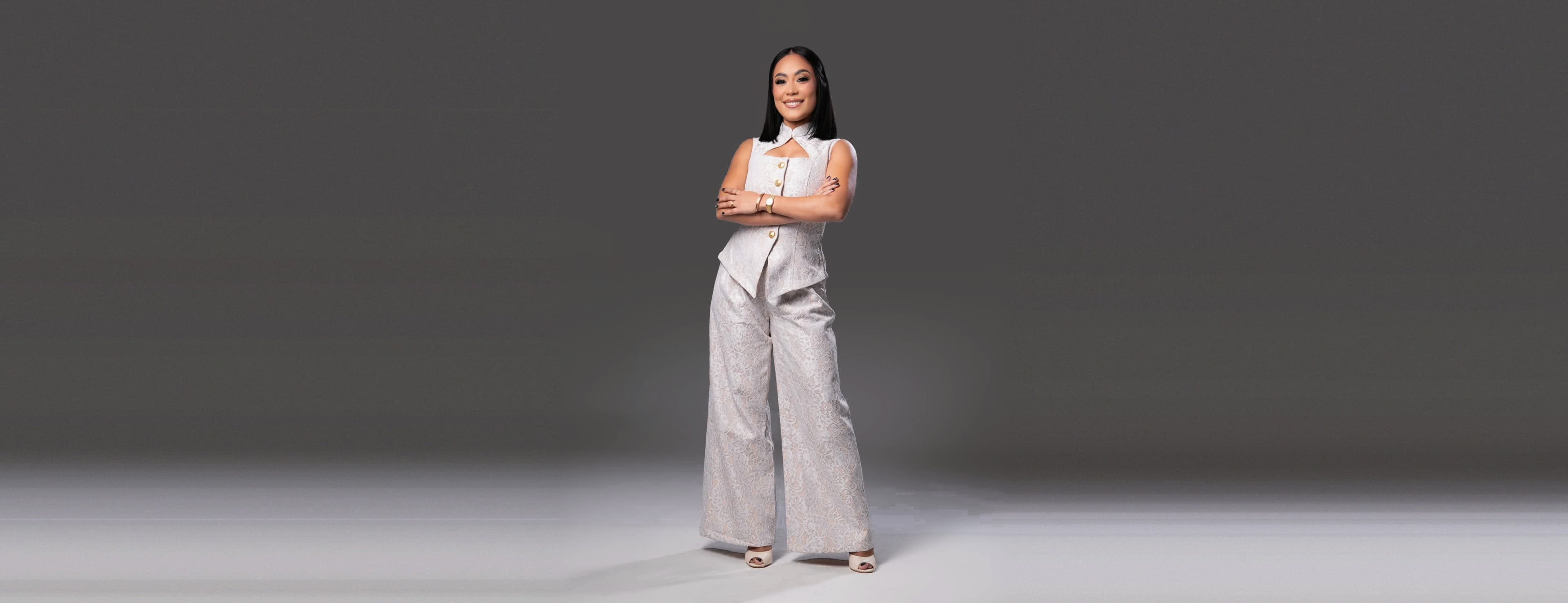 María Hernández de pie con los brazos cruzados, en un conjunto blanco de encaje con botones dorados